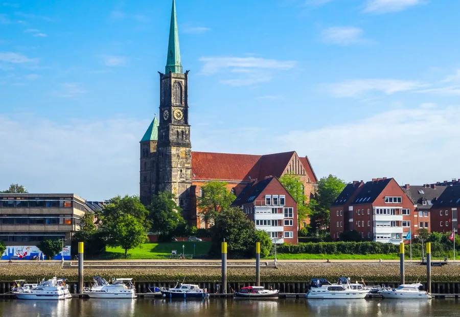 Kirchturm über einem Flussufer mit Booten